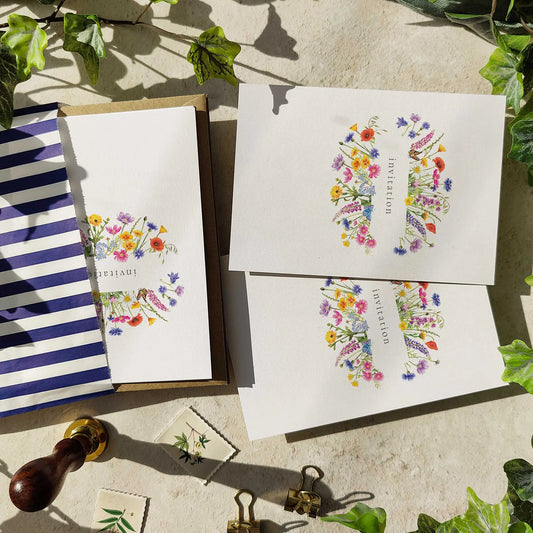 Floral stationery set with envelopes and a striped notebook on a textured surface with greenery.