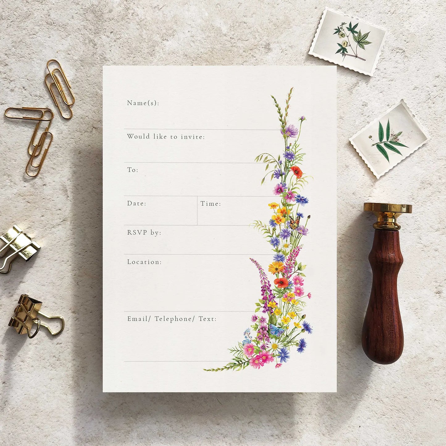 Invitation card with floral design on a textured surface with stationery items.