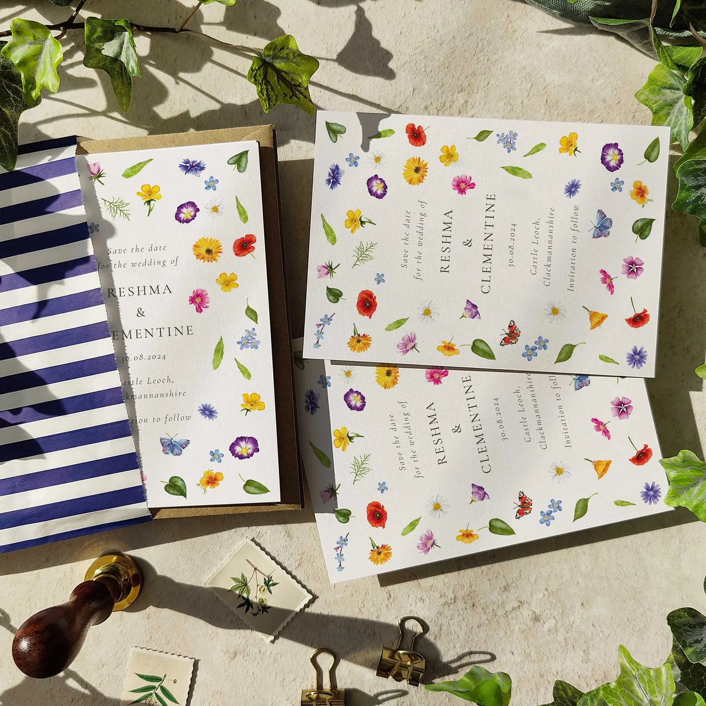 Set of floral wedding invitations on a stone surface with greenery.