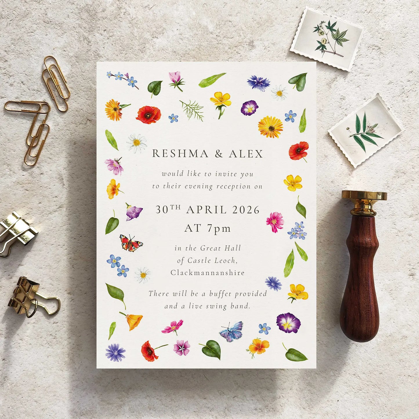 Wedding invitation card with floral design on a textured surface with stationery items.