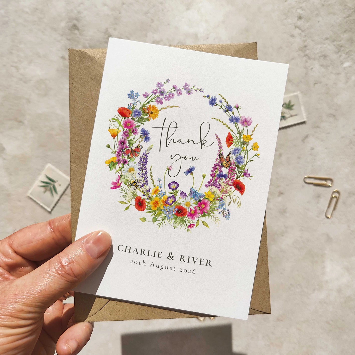 Hand holding a 'thank you' card with a floral design and personalized text on a textured surface.