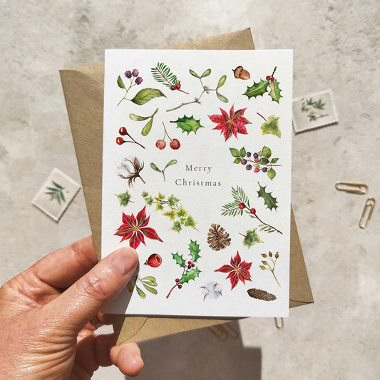 Hand holding a Christmas card with floral and botanical designs on a textured surface.