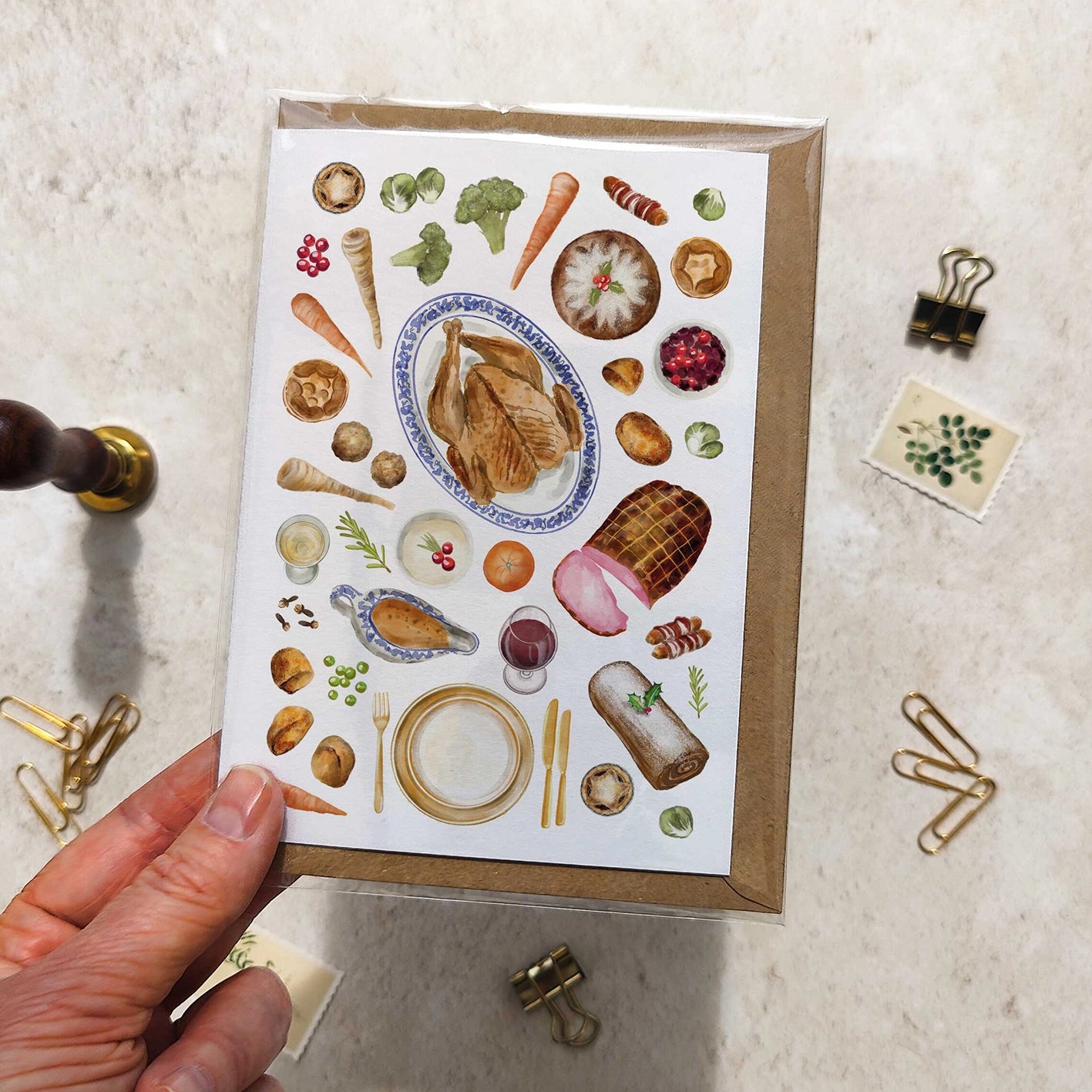 Greeting card with food illustrations held by a hand on a textured surface.