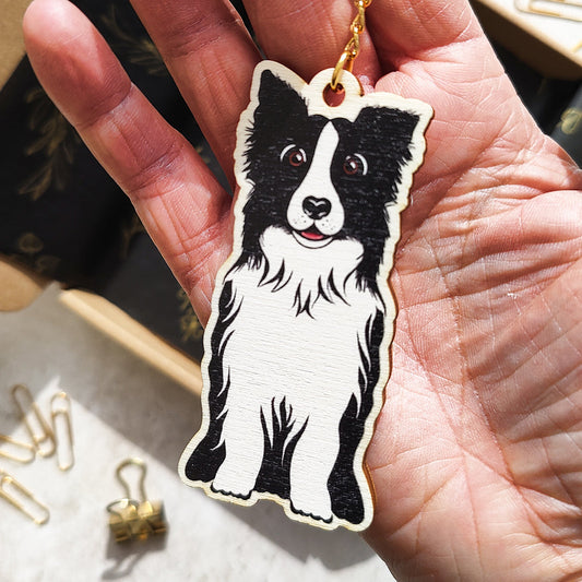Hand holding a keychain with a Collie dog design on a textured surface.