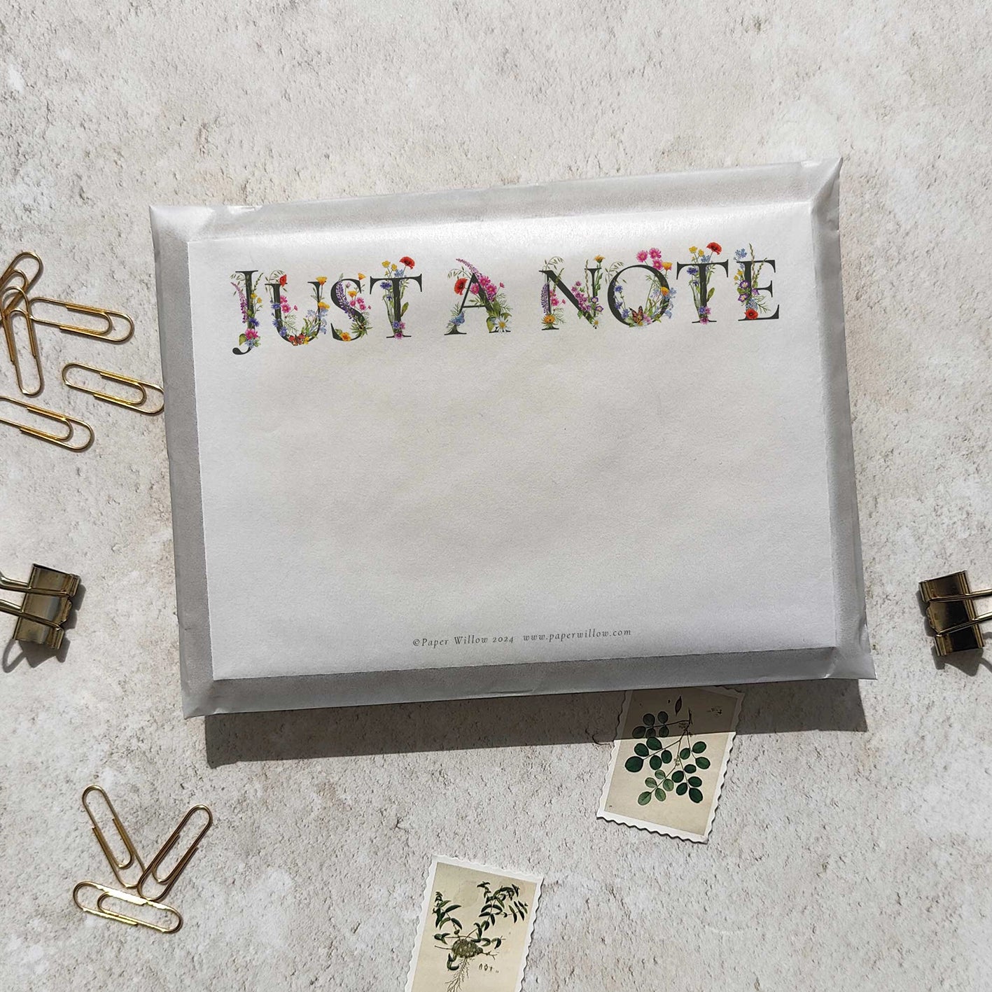 Envelopes with 'Just a Note' text on a textured surface with paper clips and small cards.