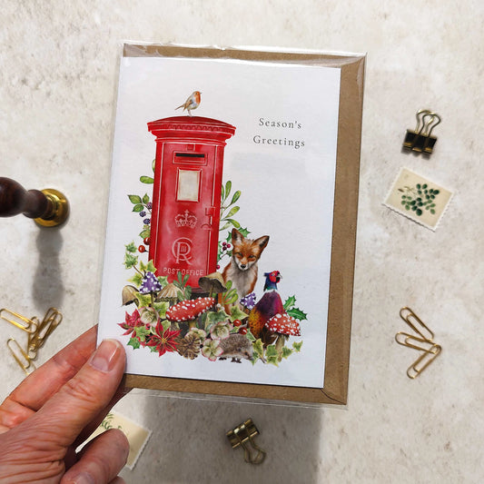 Greeting card with a red postbox and nature-themed design held by a hand on a textured surface.