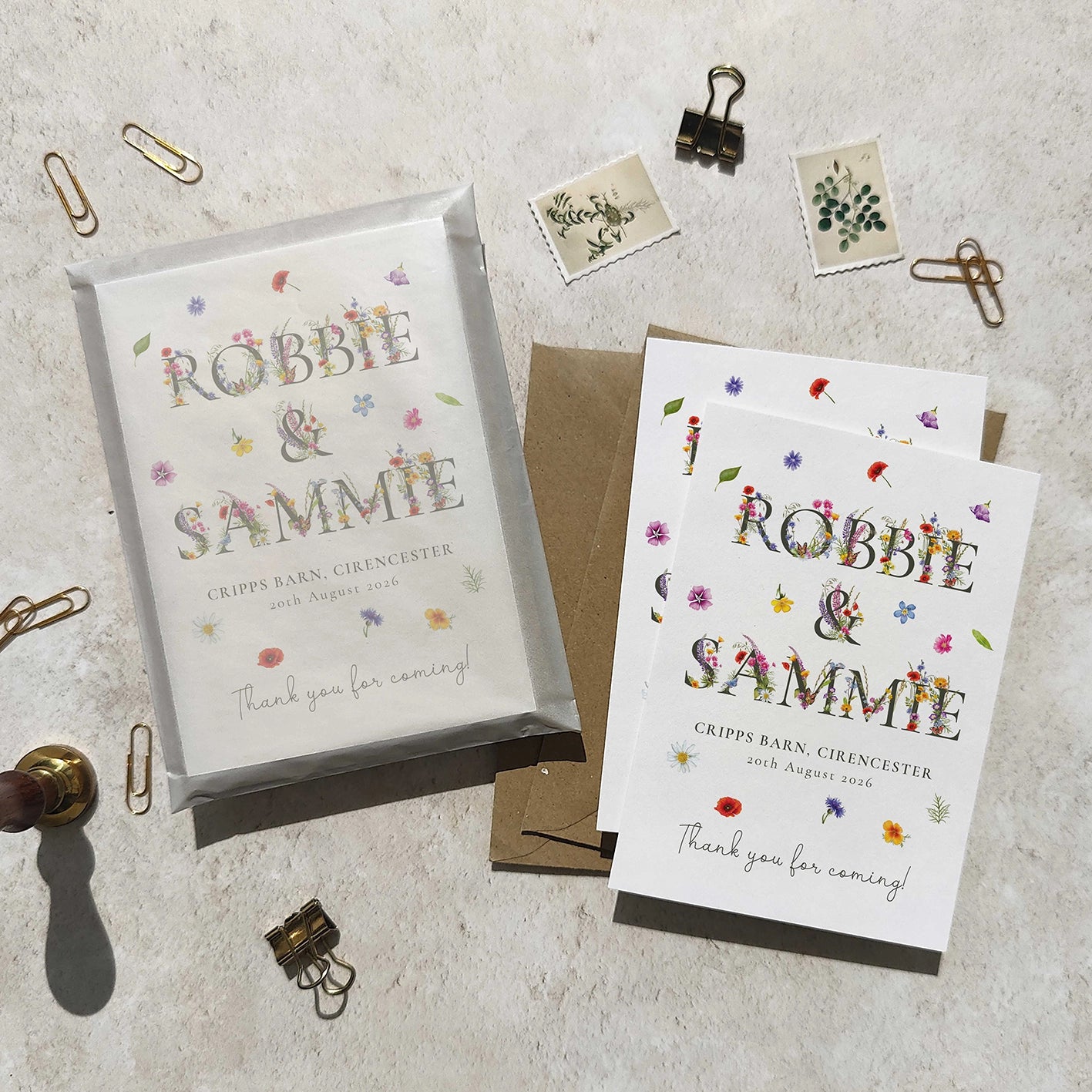 Two wedding thank you cards with floral text on a textured surface with stationery items.