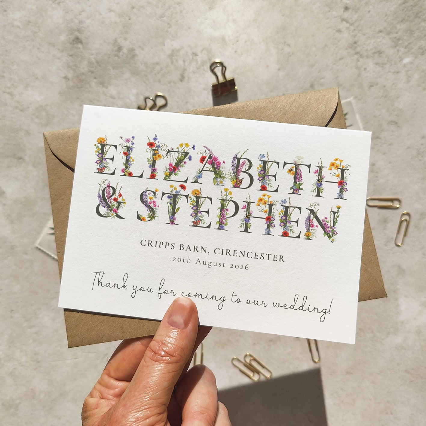 Wedding thank you card with floral text held by a hand on a textured surface