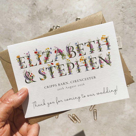 Wedding thank you card with floral text held by a hand on a concrete surface.