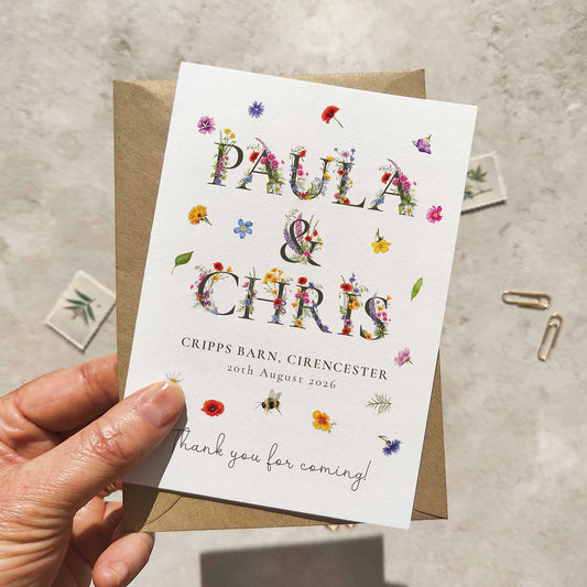 Hand holding a wedding thank you card with floral text design on a textured surface