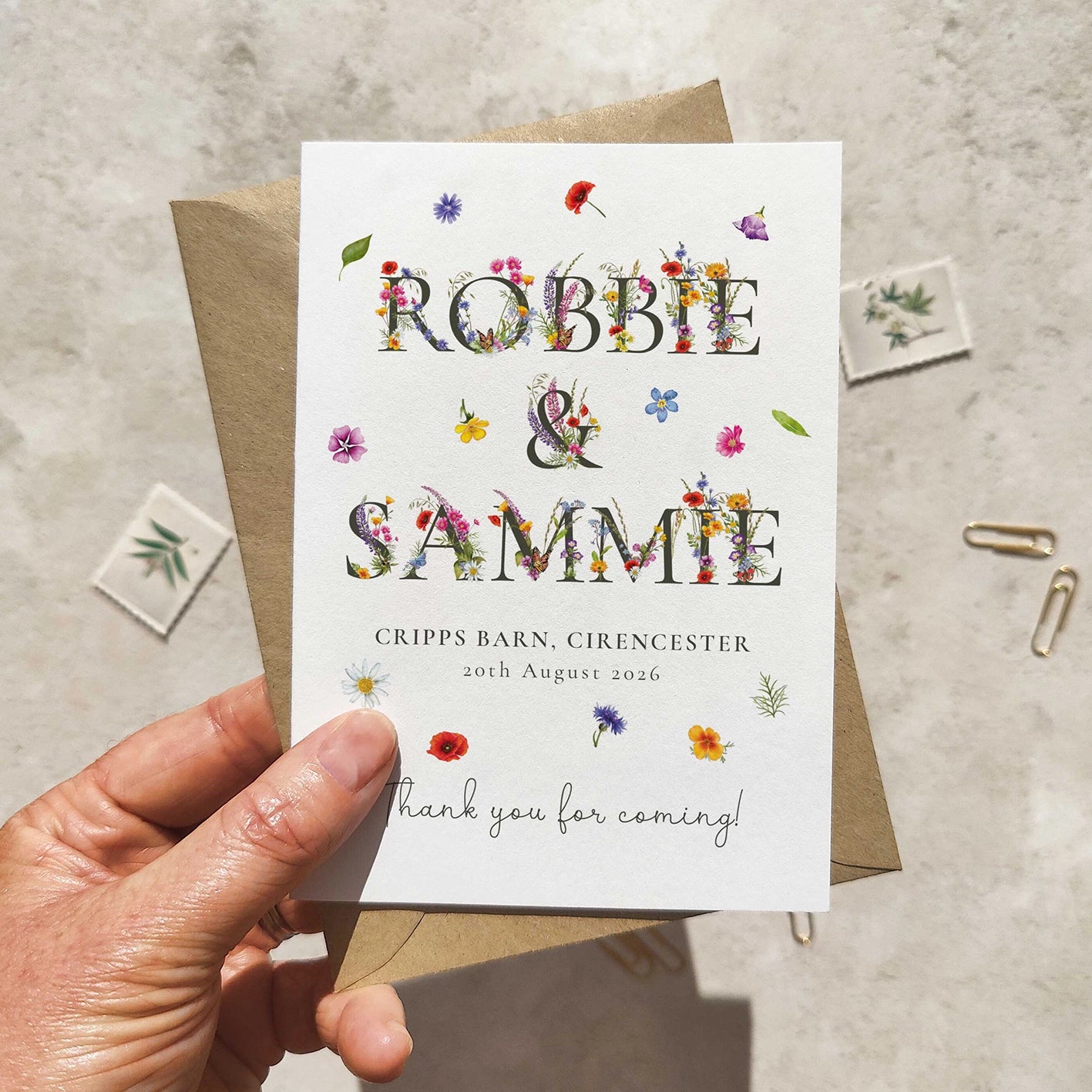 Hand holding a wedding thank you card with floral text on a textured surface