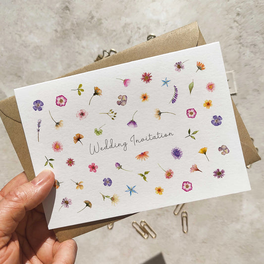 Hand holding a wedding invitation card with floral designs on a neutral background
