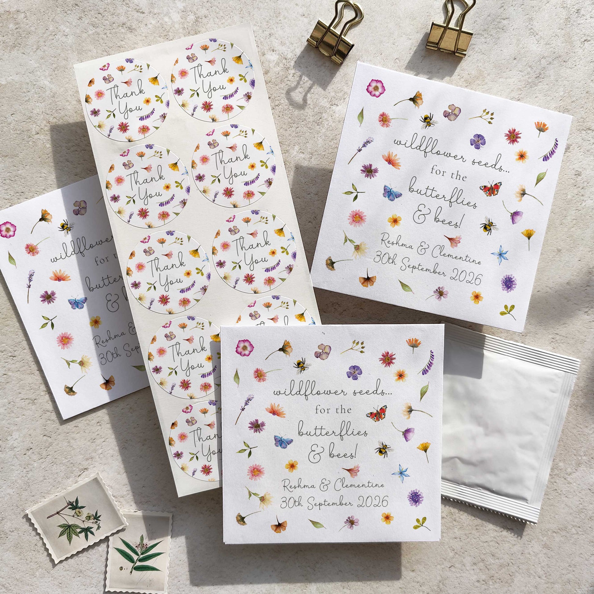 A collection of pressed wildflowers seed packets with floral designs, including personalized details such as names and dates. The packets are displayed on a textured surface with a butterfly and bee motif.