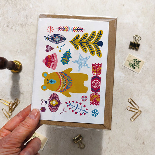 Card with colorful bear illustration held by a hand on a textured surface.