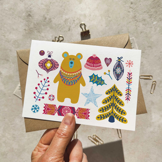 Colorful greeting card with a bear and festive elements held by a hand against a textured background.