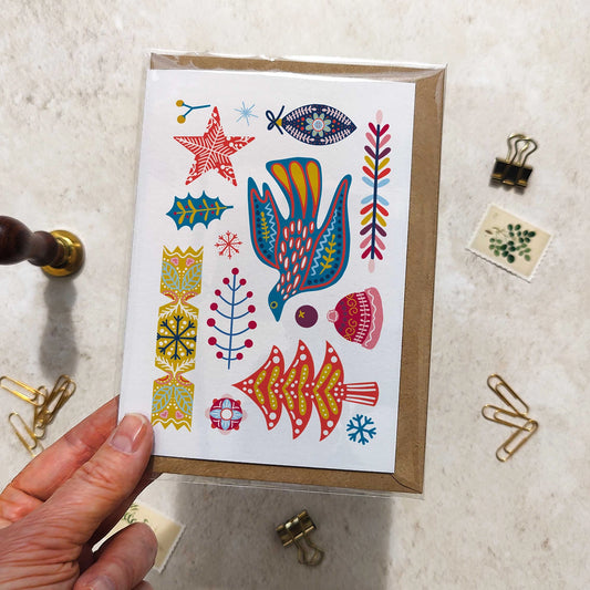 Hand holding a card with colorful illustrations of a bird, fish, and abstract shapes on a textured surface.