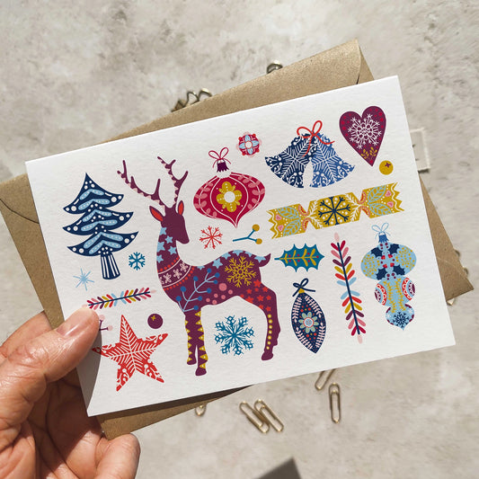 Colorful Christmas-themed card with a deer and various festive elements held by a hand.