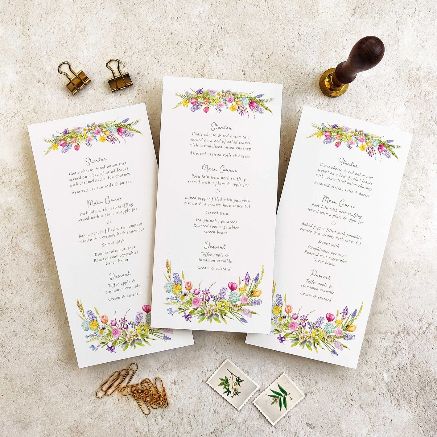 Three menu cards with spring floral designs on a textured surface.