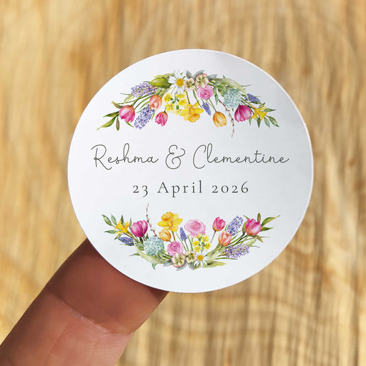 Round sticker with floral design and text held by a hand on a wooden surface