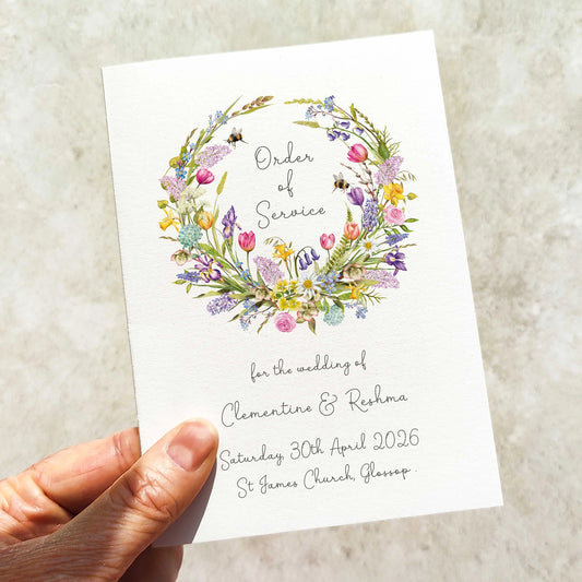 Hand holding a wedding order of service card with spring floral design