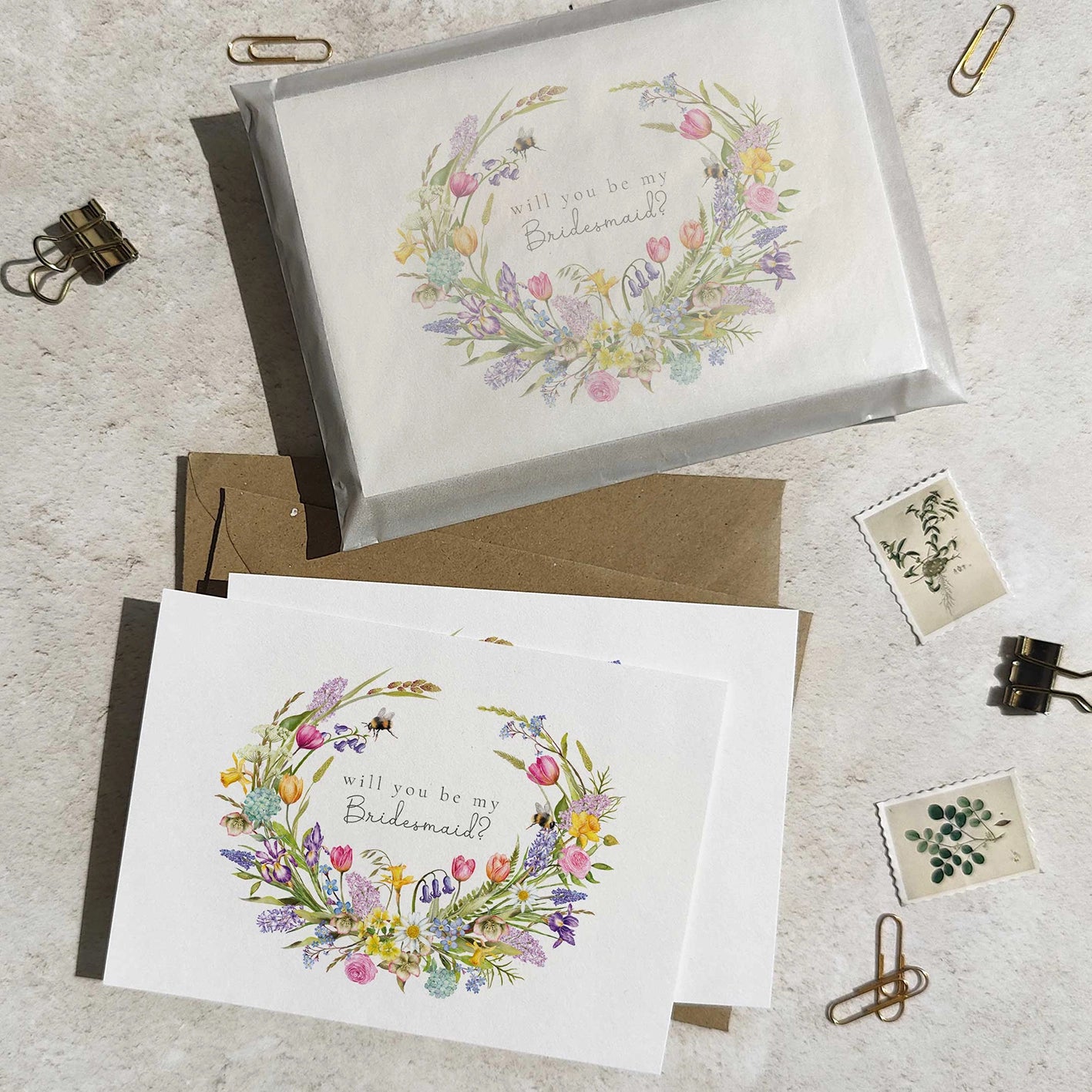 Bridesmaid cards with spring floral wreath designs and text on a textured surface.