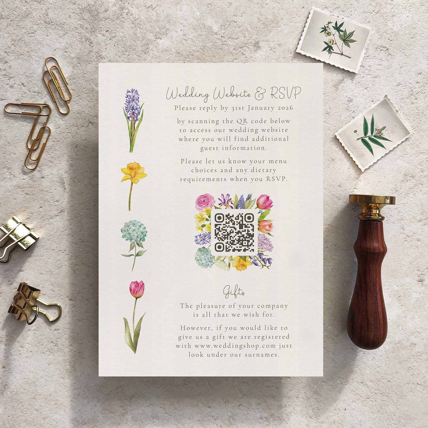 Wedding invitation card with floral designs and QR code on a textured surface with stationery items.