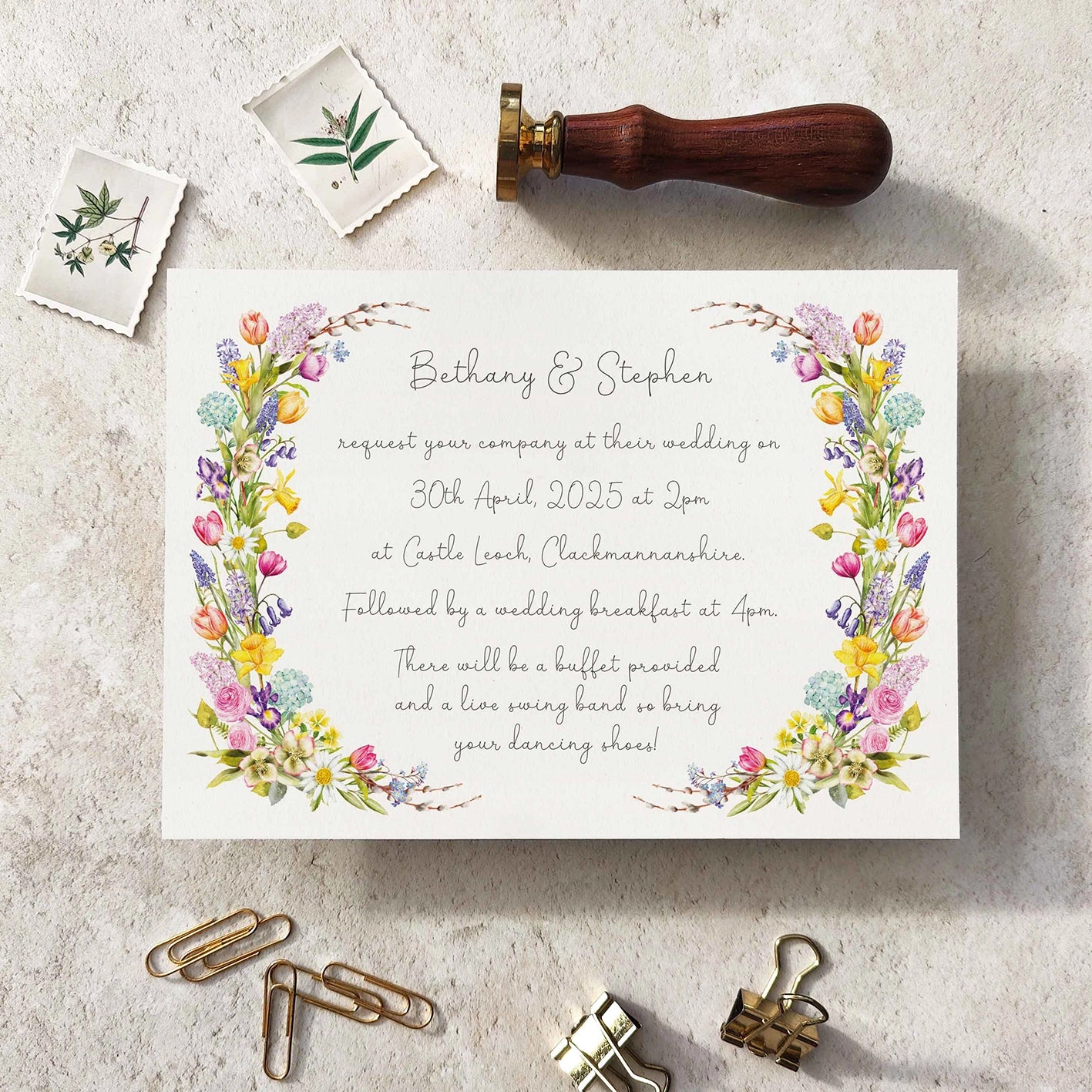 Wedding invitation card with floral design on a textured surface with stationery items.
