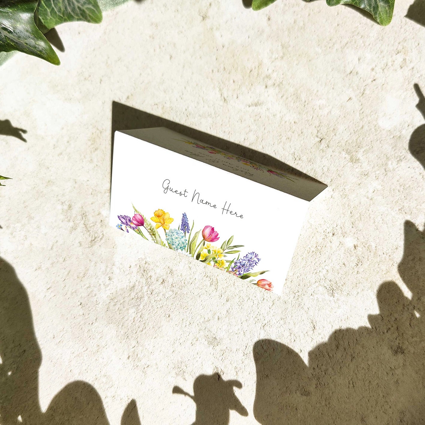Placeholder card with floral design and text 'Guest Name Here' on a textured surface.