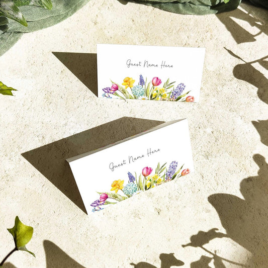 Floral place cards on a textured surface with green leaves