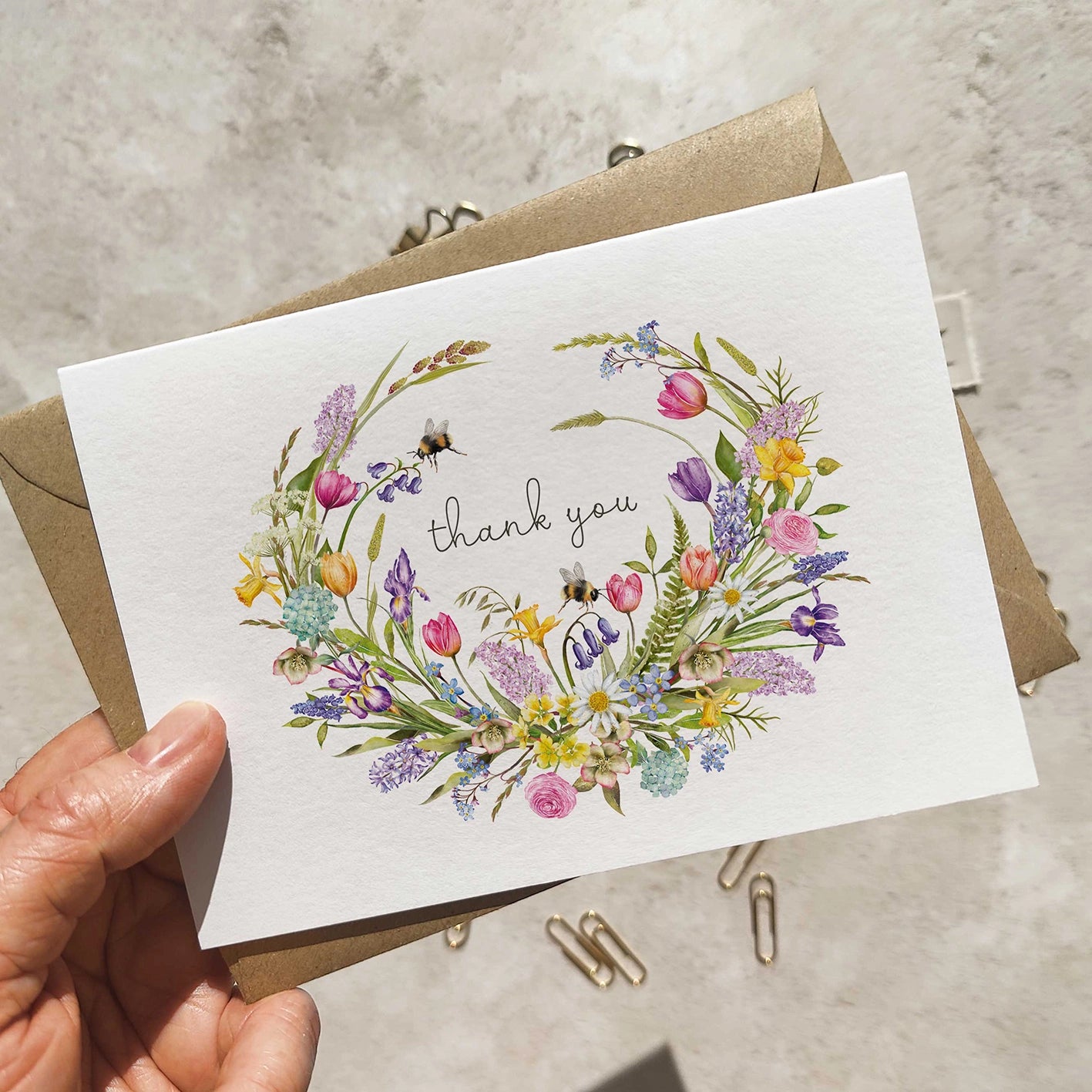 Greeting card with floral design and 'thank you' text held by a hand on a neutral background