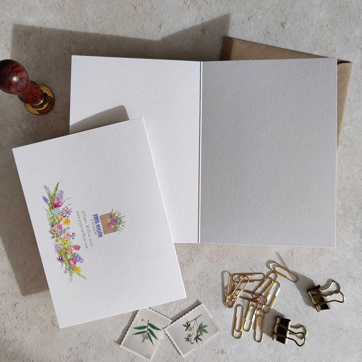 White greeting card with floral design and envelope on a textured surface with paper clips.
