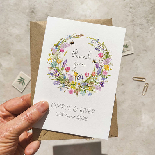 Hand holding a card with a floral wreath design and text on a textured surface.