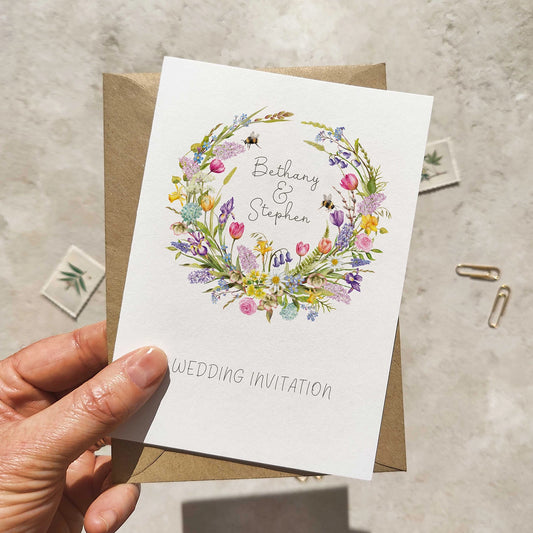 Hand holding a wedding invitation card with floral design and text on a neutral background