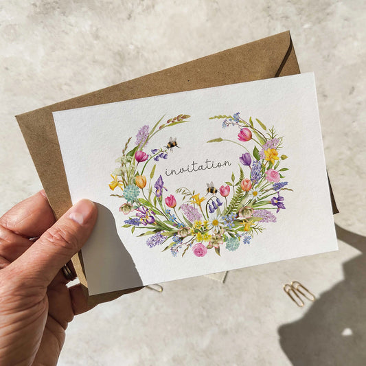 Hand holding a card with floral design and 'invitation' text, placed on a textured surface.