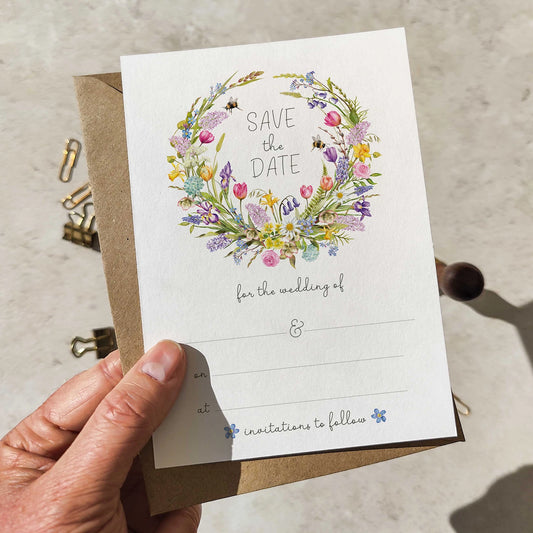 Hand holding a 'Save the Date' card with floral design and brown envelope.