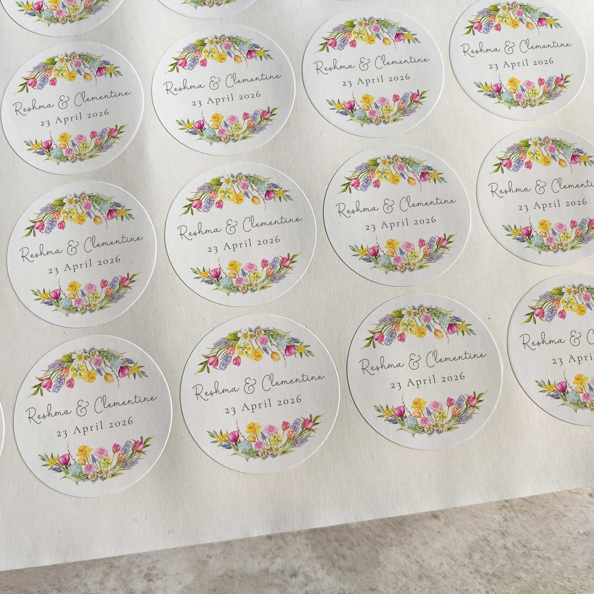 Sheet of round wedding stickers with floral designs and text on a gray surface.