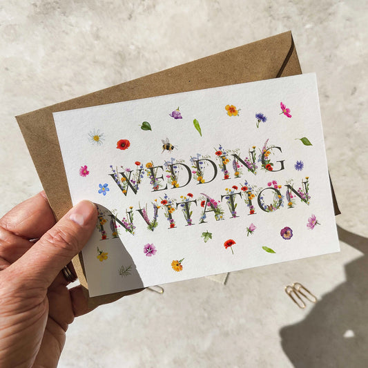 Hand holding a wedding invitation card with floral designs on a neutral background