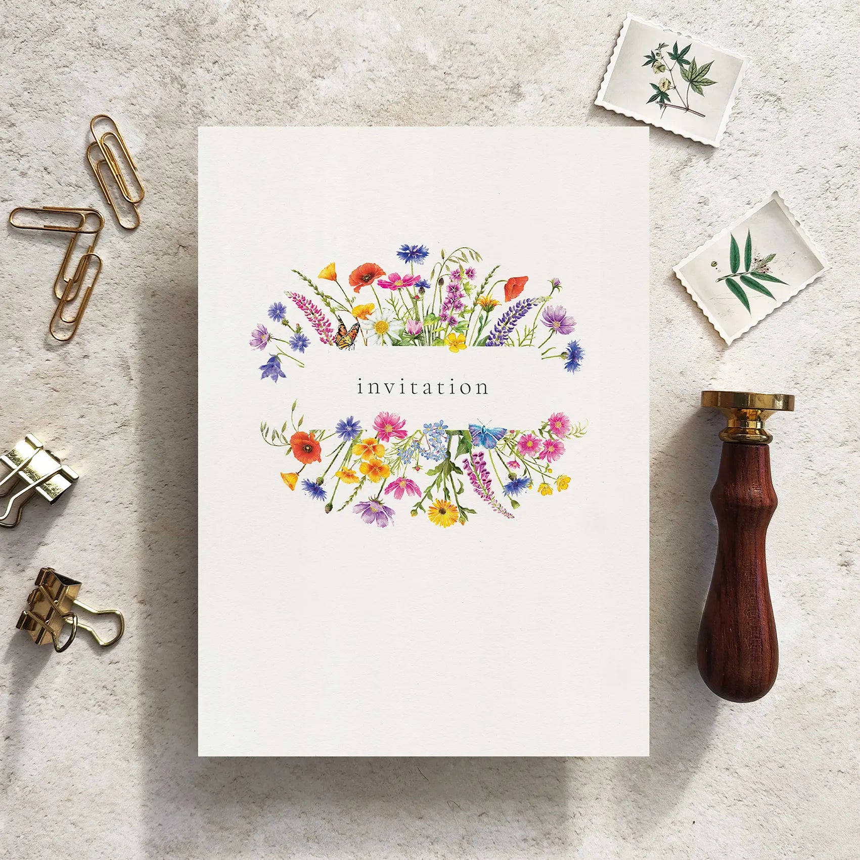 Floral invitation card on a textured surface with stationery items.