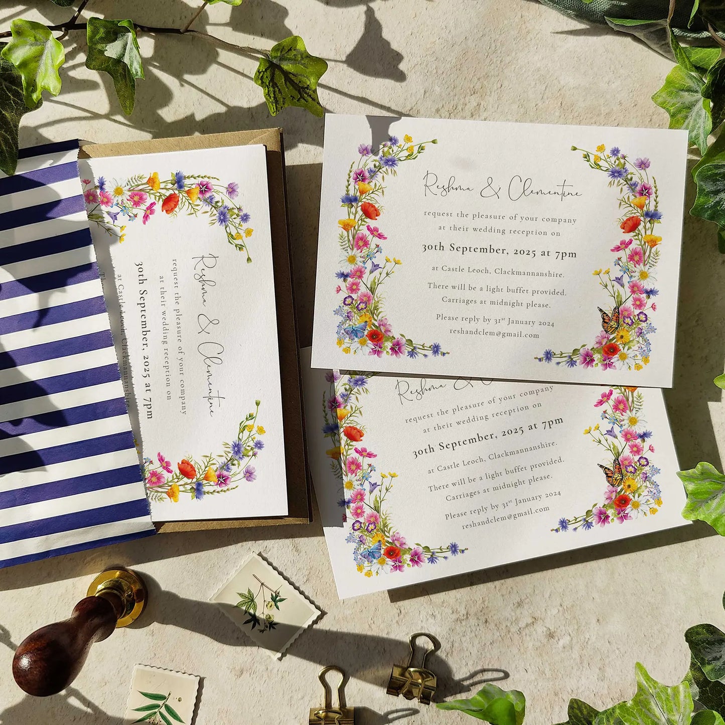 Wedding invitations with floral designs on a stone surface with greenery.