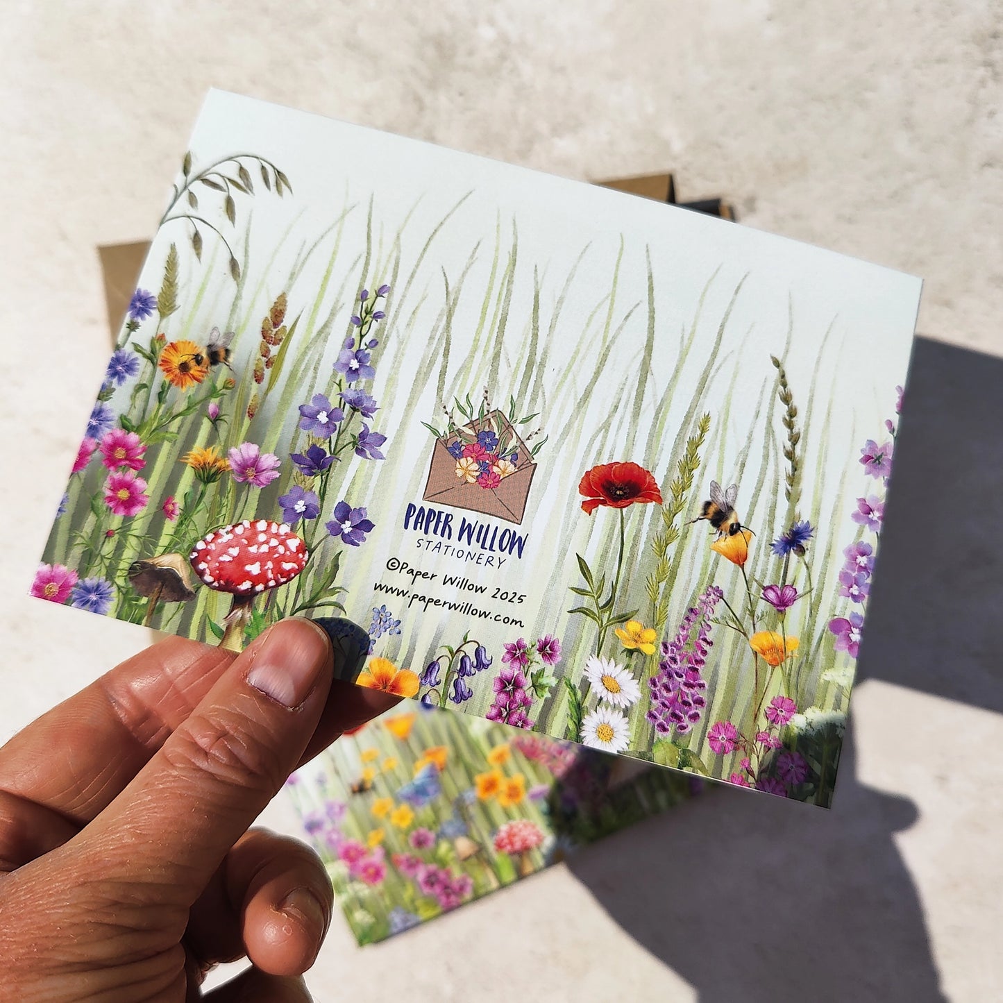 Hand holding a postcard with floral design and artist's information.